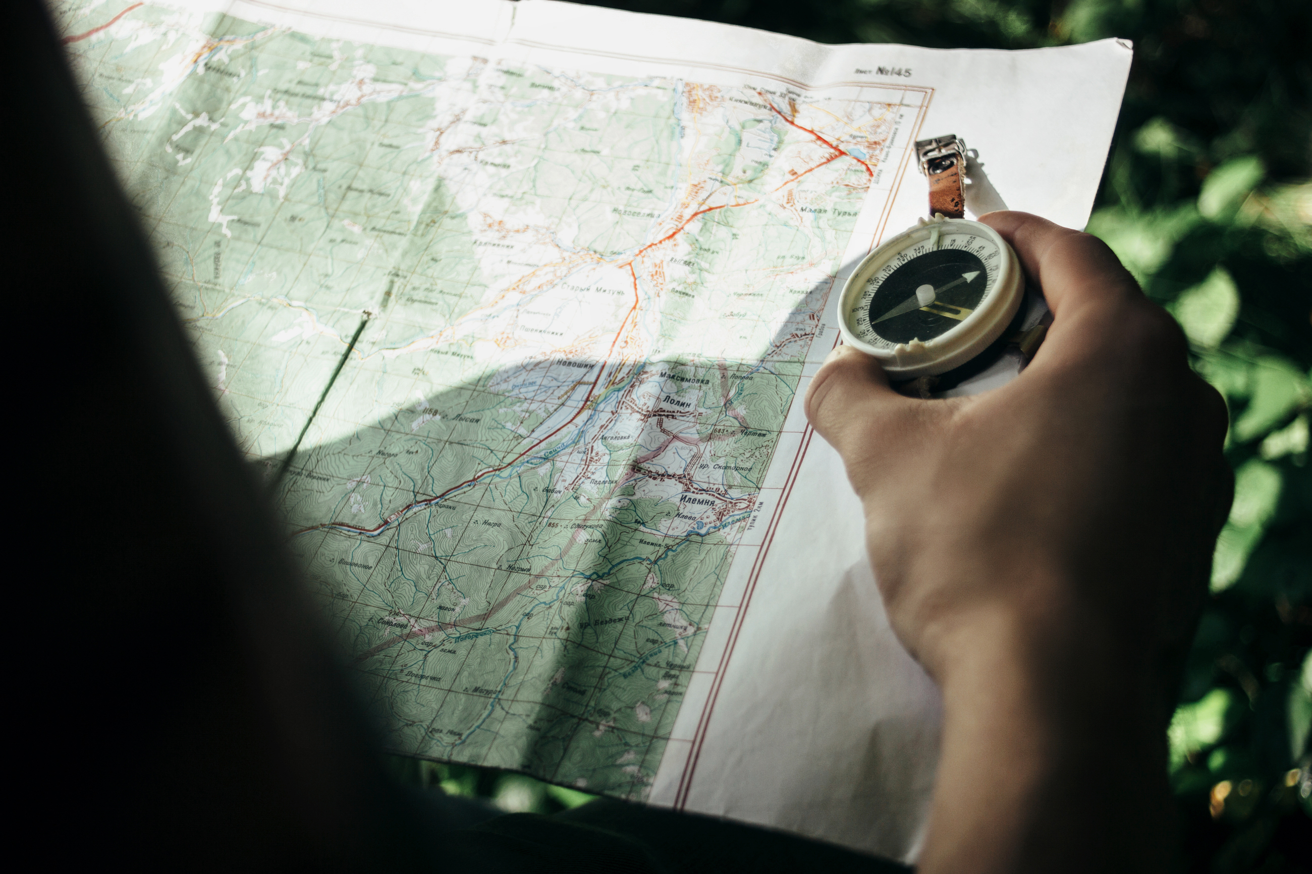 Traveler Exploring Map With Compass In Sunny Forest In The Mount